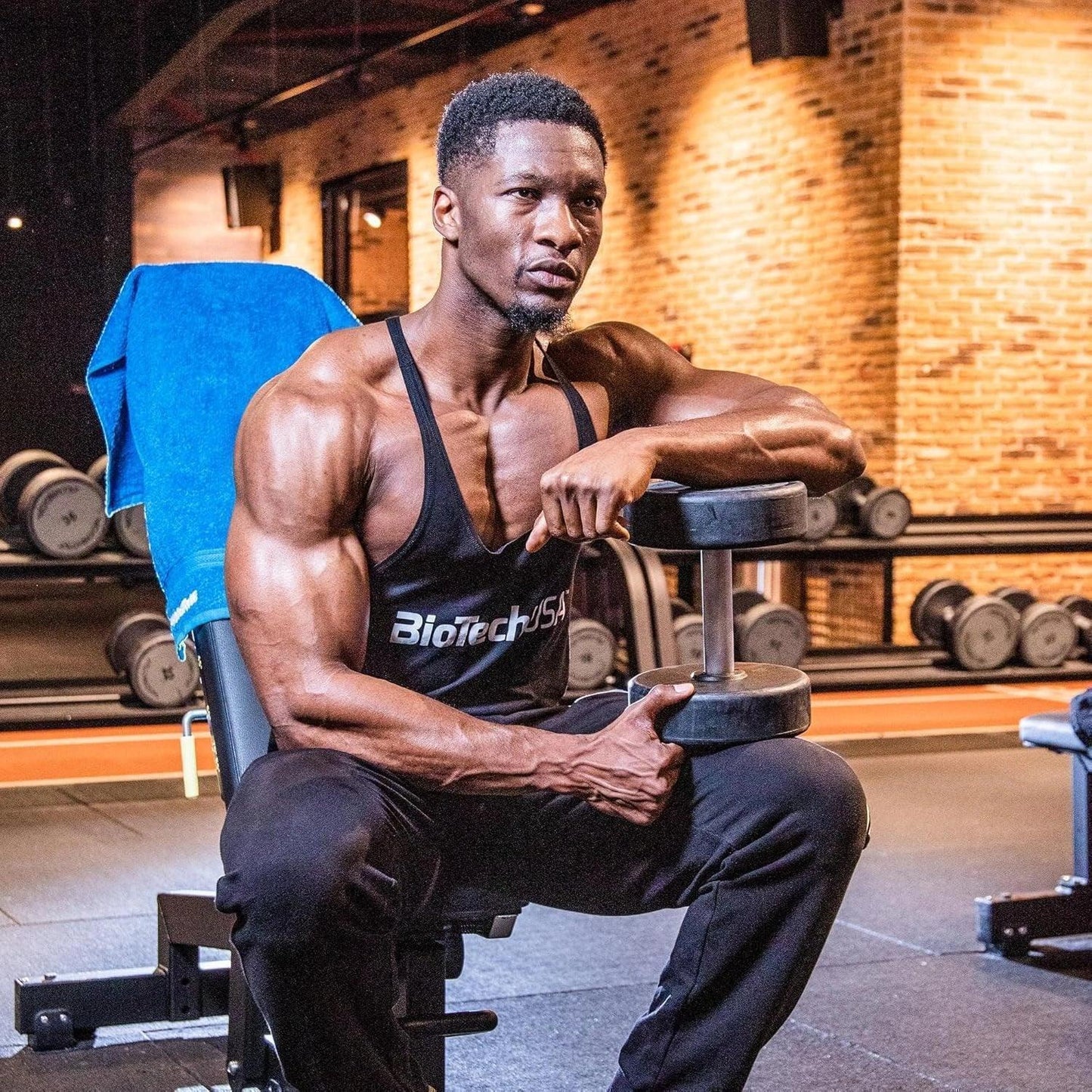 Sportlicher Mann im Fitnessstudio mit BiotechUSA Tanktop, Hantelbank und Kurzhantel