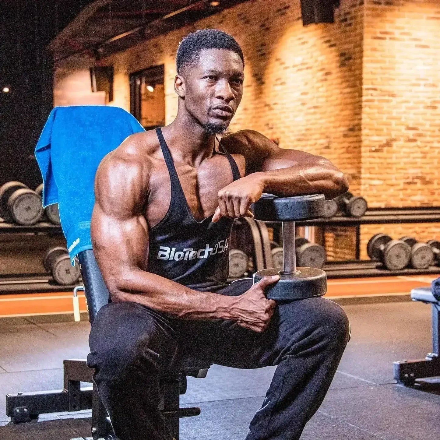 Muskelbepackter Mann in BiotechUSA Tanktop mit Hantel im Fitnessstudio, Hantelbank, Gewichte