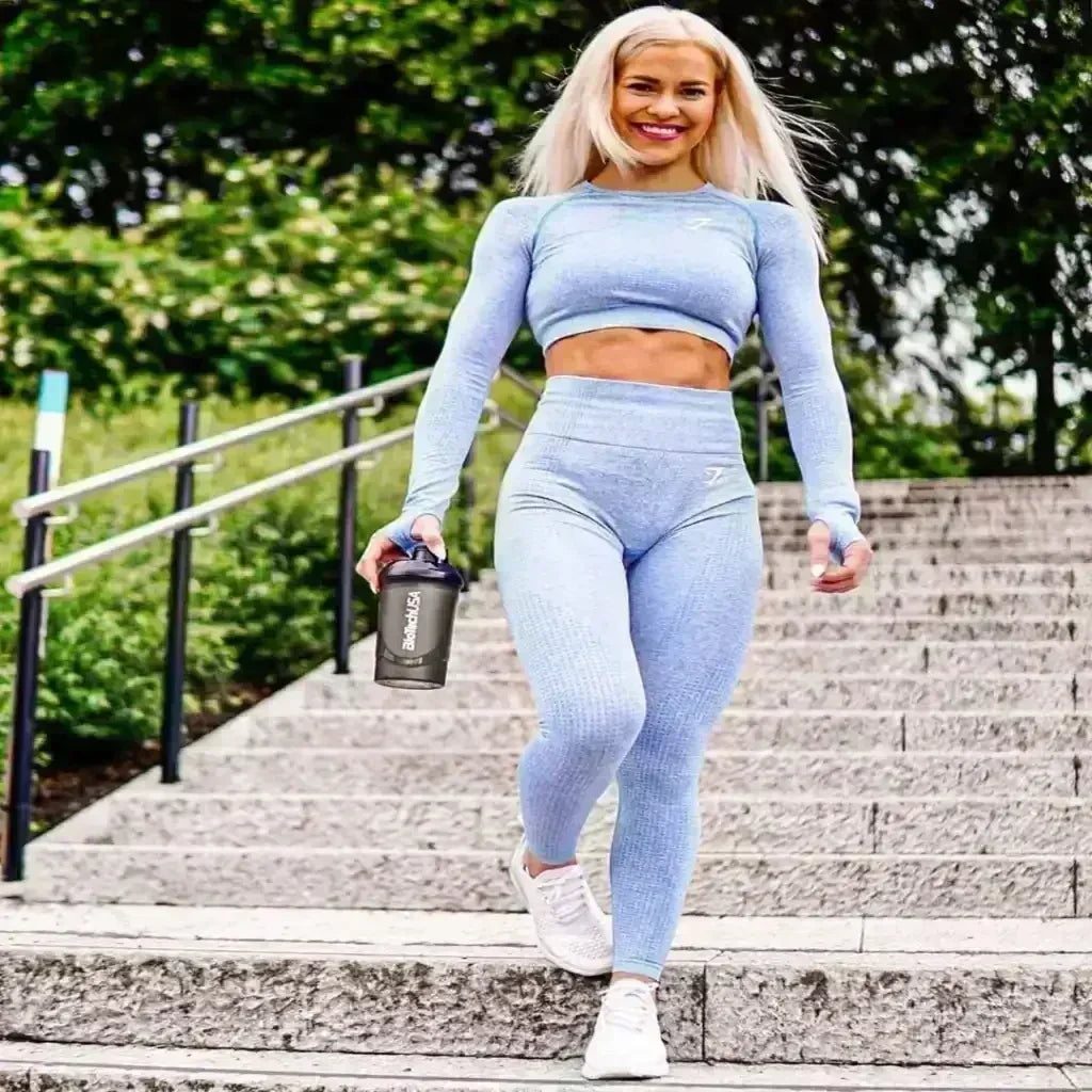 Sportliche Frau in blauer Fitnesskleidung mit Shaker auf Steintreppe im Freien