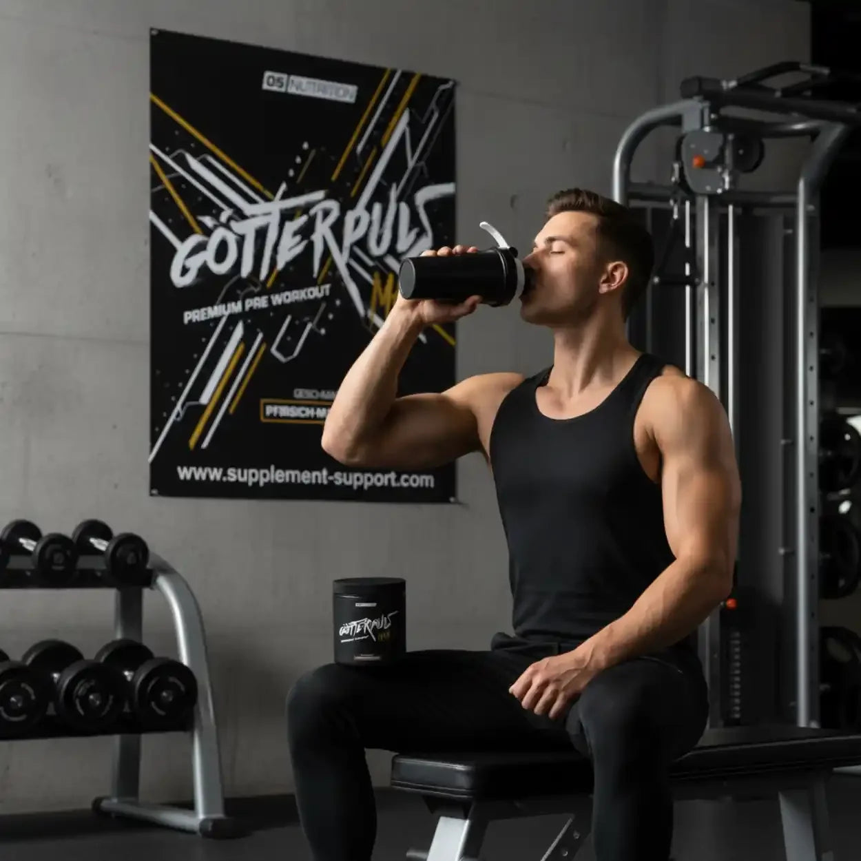 Athlet im Fitnessstudio trinkt Pre-Workout Booster, Hanteln und Götterpuls Dose sichtbar.